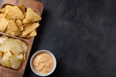 Parti çerez, cips, karanlık beton masada ahşap bir tabak içinde peynir soslu Nacho. Üstten Görünüm, kopya alanı