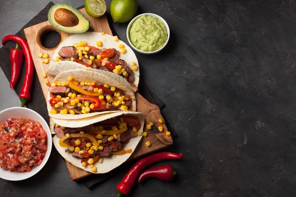 Meksykańskie tacos z marmurkowym wołowiny i warzyw na ciemnym tle kamienia. Dalej są sosy, guacamole i salsy. Widok z góry z miejsca kopii — Zdjęcie stockowe