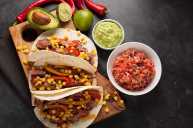 Mermer sığır eti, siyah Angus ve karanlık bir taş zemin üzerine ahşap tahta üzerinde sebze ile üç Meksikalı Taco. Soslar guacamole ve kase salsa Meksika tabak. Üstten Görünüm