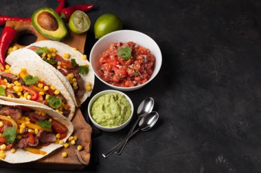 Mermer sığır eti, siyah Angus ve karanlık bir taş zemin üzerine ahşap tahta üzerinde sebze ile üç Meksikalı Taco. Soslar guacamole ve kase salsa Meksika tabak. Kopya alanı ile Üstten Görünüm