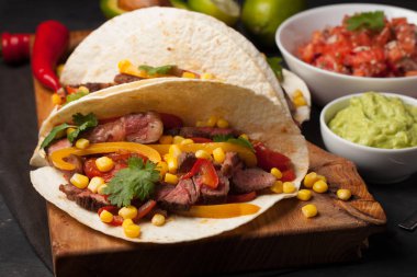 Mermer sığır eti, siyah Angus ve karanlık bir taş zemin üzerine ahşap tahta üzerinde sebze ile üç Meksikalı Taco. Soslar guacamole ve salsa kase ile Meksika yemek