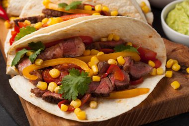 Mermer sığır eti, siyah Angus ve karanlık bir taş zemin üzerine ahşap tahta üzerinde sebze ile üç Meksikalı Taco. Soslar guacamole ve salsa kase ile Meksika yemek