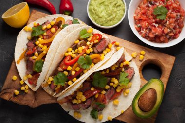 Mermer sığır eti, siyah Angus ve karanlık bir taş zemin üzerine ahşap tahta üzerinde sebze ile üç Meksikalı Taco. Soslar guacamole ve salsa kase ile Meksika yemek