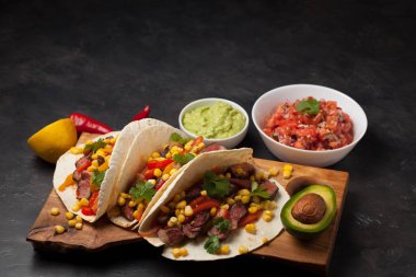 Mermer sığır eti, siyah Angus ve karanlık bir taş zemin üzerine ahşap tahta üzerinde sebze ile üç Meksikalı Taco. Soslar guacamole ve salsa kase ile Meksika yemek