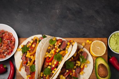Mermer sığır eti, siyah Angus ve karanlık bir taş zemin üzerine ahşap tahta üzerinde sebze ile üç Meksikalı Taco. Soslar guacamole ve kase salsa Meksika tabak. Kopya alanı ile Üstten Görünüm