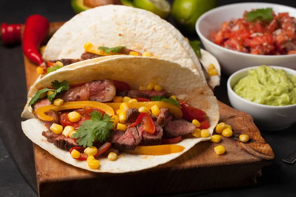 Mermer sığır eti, siyah Angus ve karanlık bir taş zemin üzerine ahşap tahta üzerinde sebze ile üç Meksikalı Taco. Soslar guacamole ve salsa kase ile Meksika yemek