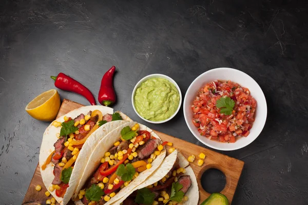 Mermer sığır eti, siyah Angus ve karanlık bir taş zemin üzerine ahşap tahta üzerinde sebze ile üç Meksikalı Taco. Soslar guacamole ve kase salsa Meksika tabak. Kopya alanı ile Üstten Görünüm