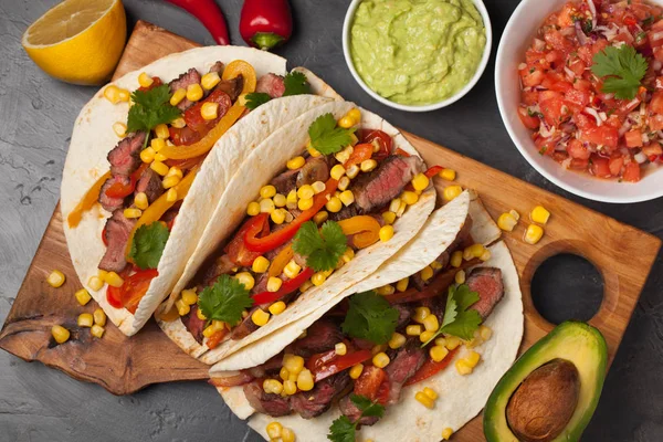 Mermer sığır eti, siyah Angus ve karanlık bir taş zemin üzerine ahşap tahta üzerinde sebze ile üç Meksikalı Taco. Soslar guacamole ve kase salsa Meksika tabak. Üstten Görünüm