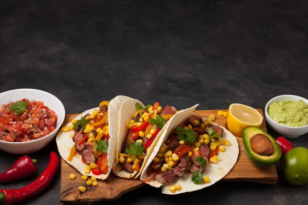 Mermer sığır eti, siyah Angus ve karanlık bir taş zemin üzerine ahşap tahta üzerinde sebze ile üç Meksikalı Taco. Soslar guacamole ve kase salsa Meksika tabak. Kopya alanı ile Üstten Görünüm