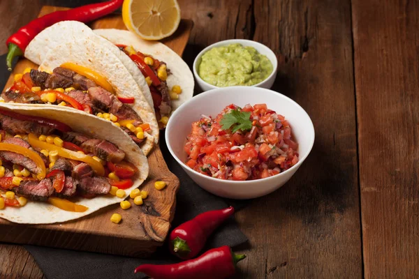 Trzy meksykańskie tacos z marmurkowym wołowiny, black Angus i warzywa na starej tabeli stylu rustykalnym. Meksykańskie danie z guacamole sosy i salsy w miski — Zdjęcie stockowe