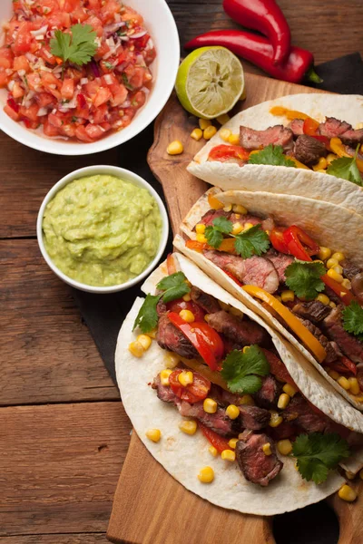 Three Mexican tacos with marbled beef, black Angus and vegetables on old rustic table. Mexican dish with sauces guacamole and salsa in bowls. top view — Stock Photo, Image