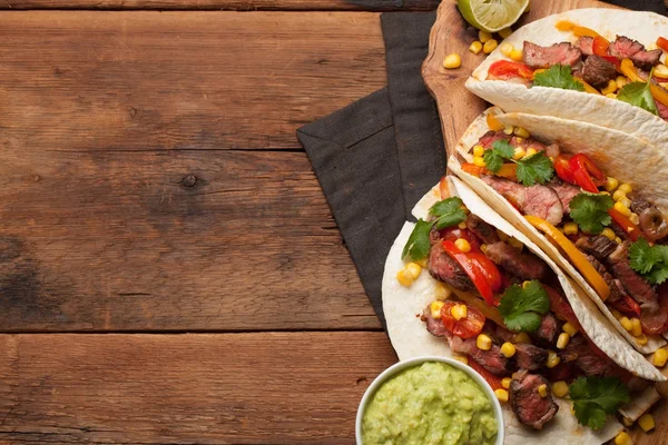 Three Mexican tacos with marbled beef, black Angus and vegetables on old rustic table. Mexican dish with sauces guacamole and salsa in bowls. Top view with copy space — Stock Photo, Image