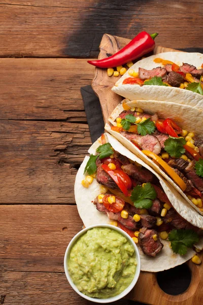 Three Mexican tacos with marbled beef, black Angus and vegetables on old rustic table. Mexican dish with sauces guacamole and salsa in bowls. top view — Stock Photo, Image