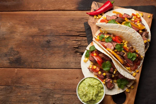 Three Mexican tacos with marbled beef, black Angus and vegetables on old rustic table. Mexican dish with sauces guacamole and salsa in bowls. Top view with copy space — Stock Photo, Image