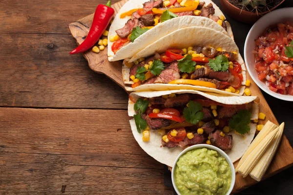 Trzy meksykańskie tacos z marmurkowym wołowiny, black Angus i warzywa na starej tabeli stylu rustykalnym. Meksykańskie danie z guacamole sosy i salsy w miskach. Widok z góry z miejsca kopii — Zdjęcie stockowe