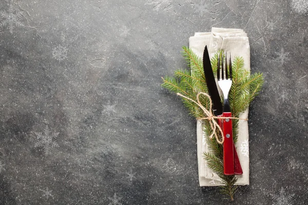 Christmas table. Cutlery with wooden handles and with a sprig of fir tied with string on a dark concrete background with copy space. Photo is decorated with snowflakes. Top view. — Stock Photo, Image