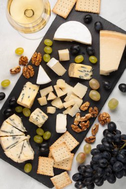 Çeşitli peynirler beyaz üzüm, ceviz, kraker ve bir taş tahta üzerinde beyaz şarap ile. Hafif bir arka plan üzerinde romantik bir tarih için yiyecek. Üstten Görünüm