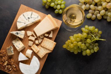 Çeşitli peynirler beyaz üzüm, ceviz, kraker ve ahşap oyun tahtası beyaz şarap ile. Karanlık bir taş zemin üzerine romantik bir tarih için yiyecek. Üstten Görünüm