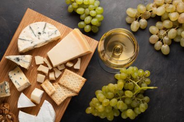 Çeşitli peynirler beyaz üzüm, ceviz, kraker ve ahşap oyun tahtası beyaz şarap ile. Karanlık bir taş zemin üzerine romantik bir tarih için yiyecek. Üstten Görünüm