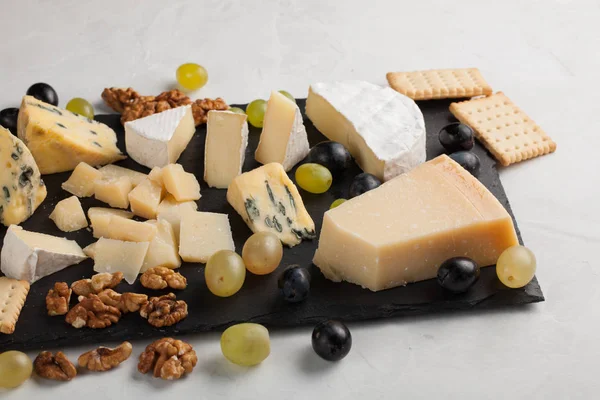 Ассорти сыров с белым виноградом, грецкими орехами, крекерами и на каменной доске. Еда для романтического свидания на светлом фоне . — стоковое фото