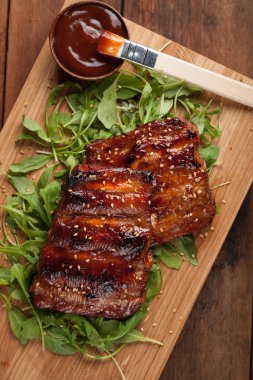 Domuz kaburga closeup Barbekü soslu ızgara ve roka bir yatak üzerinde bal karamelize. Lezzetli aperatif için bira eski ahşap arka plan üzerinde sunulması için ahşap bir gemide. Üstten Görünüm