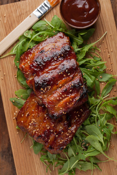 Closeup of pork ribs grilled with BBQ sauce and caramelized in honey on a bed of arugula. Tasty snack to beer on a wooden Board for submission on the old wooden background. Top view
