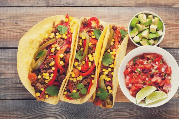 Three Mexican tacos with minced beef and mix vegetables on old rustic table. Mexican dish with sauces salsa in bowl and avocado. Spicy and hot street food. Top view — Stock Photo, Image