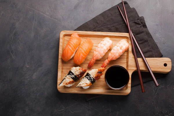Zestaw sushi z łososiem, krewetkami i węgorz z miski sos sojowy i drewniane pałeczki do jedzenia na płycie. Pysznych potraw japońskich na ciemnym tle kamienia. Widok z góry z miejsca kopii — Zdjęcie stockowe