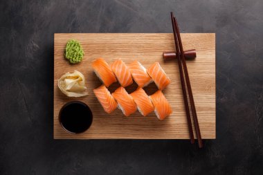 Klasik bir Philadelphia rulo wasabi, zencefil ve soya sosu ile ahşap bir gemide. Somon, Philadelphia peyniri, salatalık, avokado. Japon suşi karanlık bir taş zemin üzerine. Üstten Görünüm