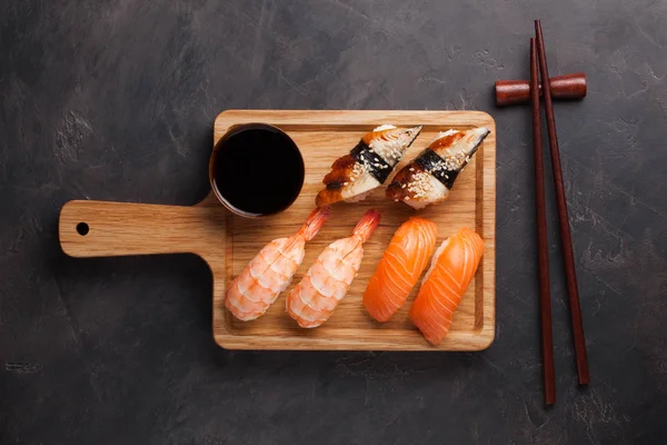 Un set di sushi con salmone, gamberetti e anguilla con una ciotola di salsa di soia e bacchette di legno su una tavola di legno. Delizioso cibo giapponese su uno sfondo di pietra scura. Vista dall'alto — Foto Stock