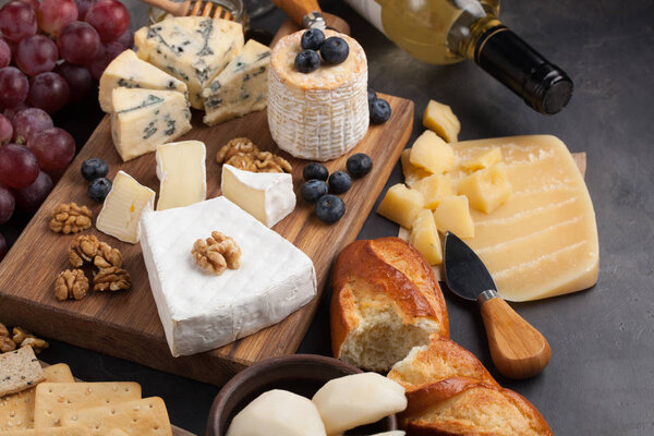 Tasting cheese dish on a dark stone plate. Food for wine and romantic date, cheese delicatessen on a black concrete background