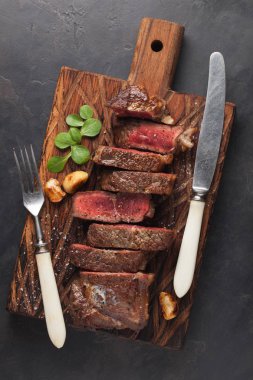 Closeup biftek new York sığır ırkları kara Angus otlar, sarımsak ve ahşap bir tahta üzerine tereyağı ile yemeye hazır. Bitmiş çanak taş karanlık bir arka plan akşam yemeği için. Üstten Görünüm