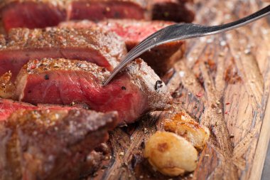 Closeup biftek new York sığır ırkları kara Angus otlar, sarımsak ve ahşap bir tahta üzerine tereyağı ile yemeye hazır. Bitmiş yemek yemek için. Bir çatal bile delip biftek bitmiş parça