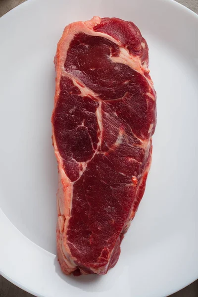 Bife cru marmoreado em um prato branco. Bife de Nova Iorque. Vista superior close-up — Fotografia de Stock