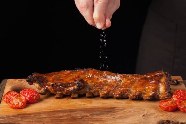 Şef tuz Domuz kaburga, yemeye hazır bir eski ahşap masanın üzerinde yatan sprinkles. Bir adam siyah bir arka plan kopya alanı ile bira için atıştıracak bir şeyler hazırlar