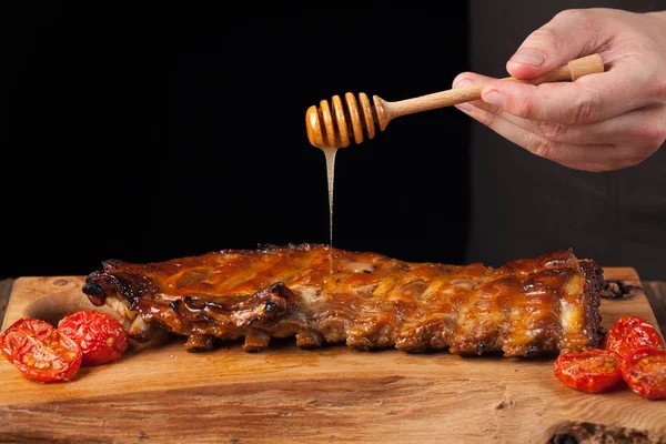 Matlagning fläsk revben revbensspjäll med honung söt sås på mörk trä bakgrund. Kocken häller honung revbensspjäll. Med kopia utrymme — Stockfoto