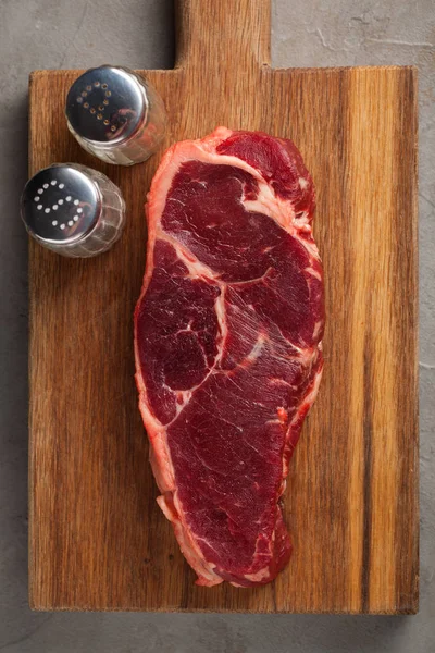 Νωπό βόειο κρέας μαρμάρινα μπριζόλα με vintage λευκό μαχαιροπίρουνα σε παλιό πέτρινο φόντο. Ένα κομμάτι κρέας σε ένα ξύλινο ταμπλό. Νέας Υόρκης μπριζόλα. Το Top view με αντίγραφο χώρου — Φωτογραφία Αρχείου