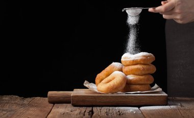 Baker siyah arka plan üzerine toz şeker tatlı çörek sprinkles. Lezzetli, ama sağlıksız yemek kopya alanı eski ahşap tablo