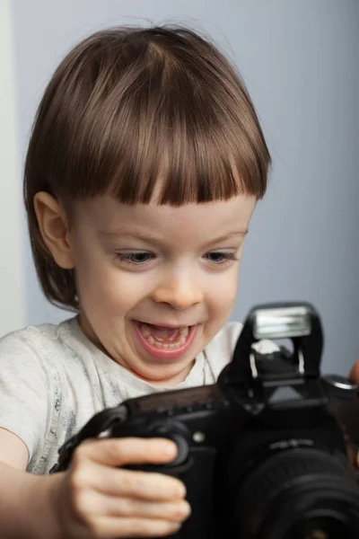 Beautiful child in with professional camera. Little boy with long blond hair photographing in the Studio. He looks at the resulting images on the camera and is happy — Stock Photo, Image