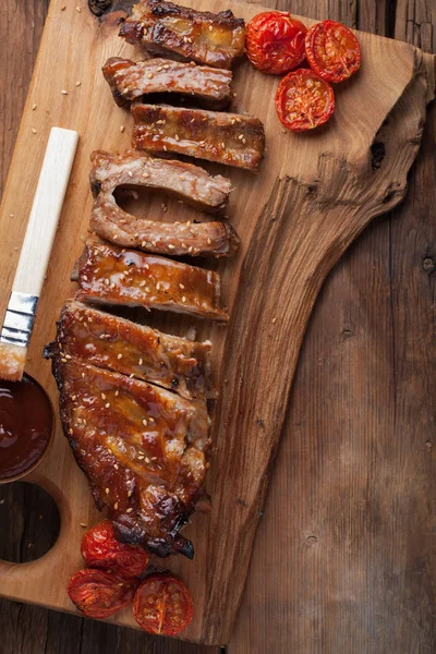 Costeletas de porco em molho de churrasco e tomate assado mel em uma tábua de madeira. Um ótimo lanche para cerveja em uma mesa de madeira rústica. Vista superior — Fotografia de Stock