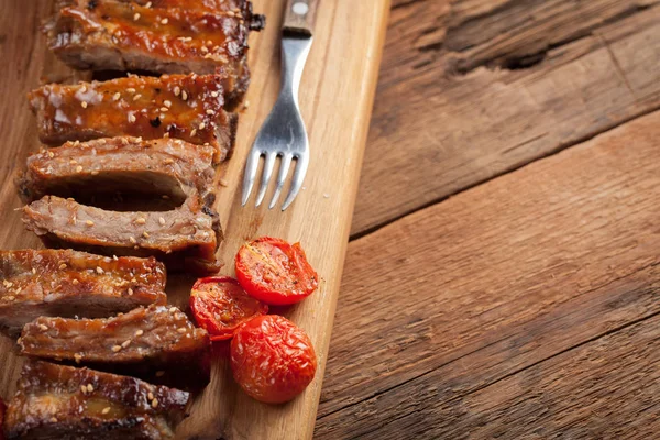 Pork ribs in barbecue sauce and honey roasted tomatoes on a wooden board. A great snack to beer on a rustic wooden table. Top view with copy space — Stock Photo, Image