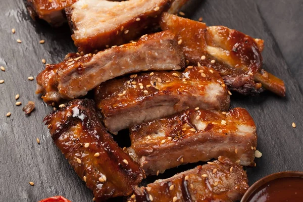 Pork ribs in barbecue sauce and honey roasted tomatoes on a black slate dish. A great snack to beer on a black stone background. Top view — Stock Photo, Image
