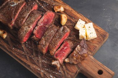 Closeup biftek new York sığır ırkları kara Angus otlar, sarımsak ve ahşap bir tahta üzerine tereyağı ile yemeye hazır. Bitmiş çanak taş karanlık bir arka plan akşam yemeği için. Üstten Görünüm