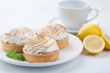 Limon beze vintage beyaz tabak ve bardak çay taş masanın üzerine ile tartlets. Açık mavi arka planı üzerinde lezzetli tedavi