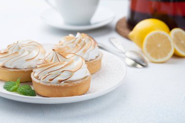 Limon beze vintage beyaz tabak ve bardak çay taş masanın üzerine ile tartlets. Açık mavi arka planı üzerinde lezzetli tedavi