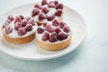 Beyaz vintage tabakta lezzetli ahududu tartlets. Tatlı ışık mavi bir arka plan üzerinde tedavi