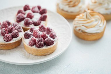 Ahududu ve lezzetli limon beze beyaz vintage tabakta ile tartlets. Tatlı ışık mavi bir arka plan üzerinde tedavi