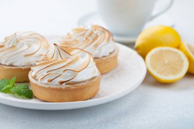 Limon beze vintage beyaz tabak ve bardak çay taş masanın üzerine ile tartlets. Açık mavi arka planı üzerinde lezzetli tedavi