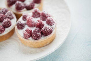 Beyaz vintage tabakta lezzetli ahududu tartlets. Tatlı ışık mavi bir arka plan üzerinde tedavi