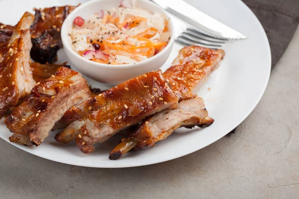 Costolette di maiale alla griglia in salsa barbecue e miele con crauti su piatto bianco. Spuntino a birra su un tavolo di pietra leggero — Foto Stock